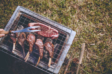 Herb seasoning Lamb rack and beef grilled on charcoal stove outdoor on the grass ground with kitchen equipment knife and fork.の写真素材