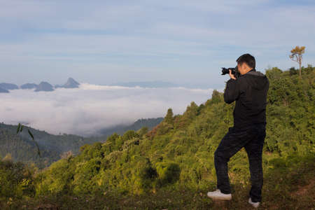 a male photographer with his camera shooting at the hill top with sea of fog over the mountainの写真素材