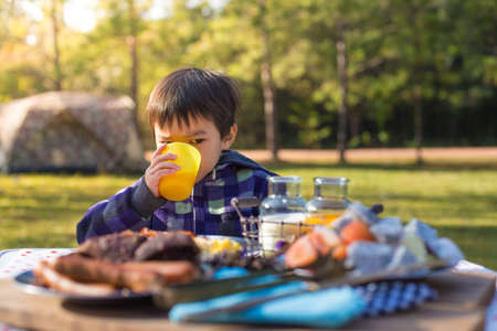 An Asian cute young boy eating breakfast outdoor at camping site in nature sunlight with a tent at the background.の写真素材