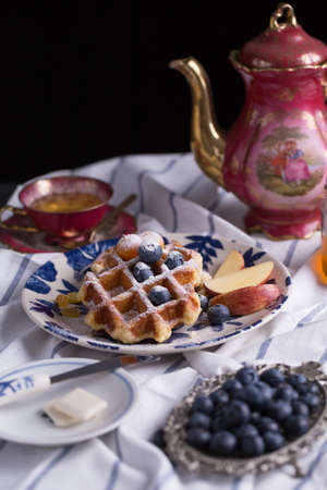 Blueberry apple waffle with honey set on a dish decorated with fresh blueberry, apple, tea pot set ready to serve.の写真素材