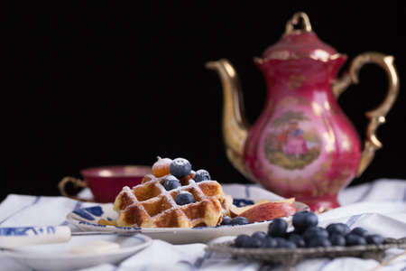 Blueberry apple waffle with honey set on a dish decorated with fresh blueberry, apple, tea pot set ready to serve.の写真素材