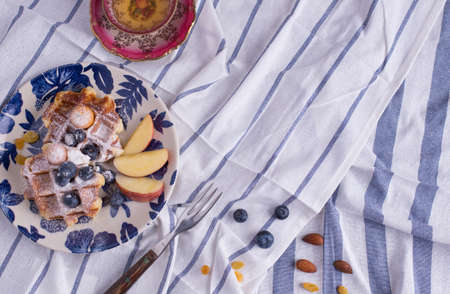 Blueberry apple waffle with honey set on a dish decorated with fresh blueberry, apple, tea pot with copy space.の写真素材