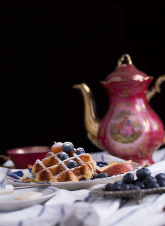 Blueberry apple waffle with honey set on a dish decorated with fresh blueberry, apple, tea pot with copy space.の写真素材