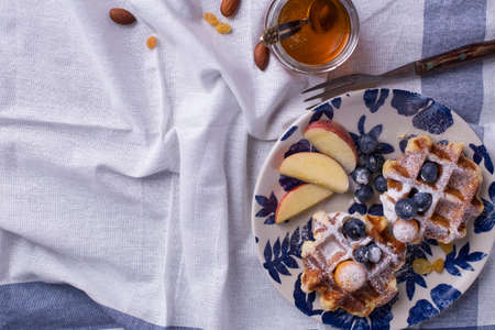 Blueberry apple waffle with honey set on a dish decorated with fresh blueberry, apple, tea pot with copy space.の写真素材