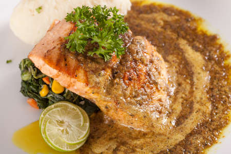 A nice dish of salmon steak served with mashed potato,lemon, sautÃ© spinach and sauce on wood backgroundの写真素材