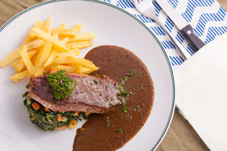 A dish of beef steak served with pepper brown sauce, spinach sautÃ© and french fries in a decorated dish with copy spaceの写真素材