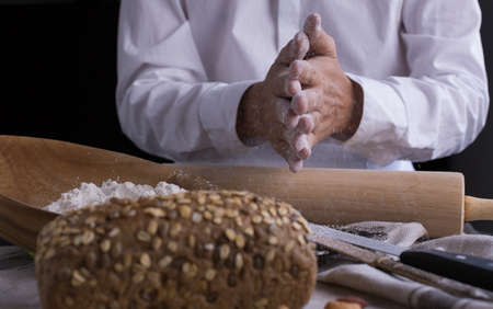 A male chef's hand present and cutting whole grain bread with gold knife and pouring flour.の写真素材