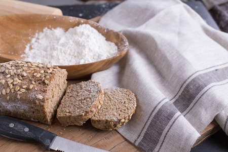 Whole grain wheat bread set on nice fabric brown background decorated with flour bowl and a bakery...