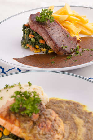 A nice dish beef and salmon steak served with mashed potato,lemon, saute spinach and sauce on wood backgroundの写真素材