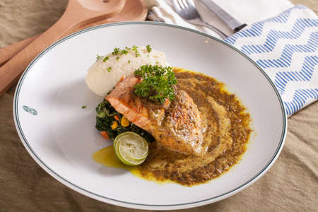 A nice dish of salmon and beef steak served with mashed potato,lemon, saute spinach and sauce on  background with wooden utensils.の写真素材