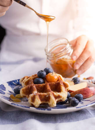 Blueberry apple waffle with honey set on a dish with a chef's hand holding spoon for a jar of honey ready to serve.の写真素材