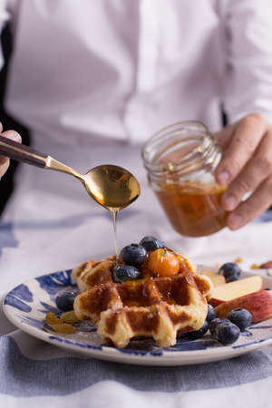 Blueberry apple waffle with honey set on a dish with a chef's hand holding spoon for a jar of honey ready to serve.の写真素材