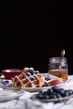 Blueberry apple waffle with honey set on a dish decorated with fresh blueberry, apple, tea pot with copy space.の写真素材