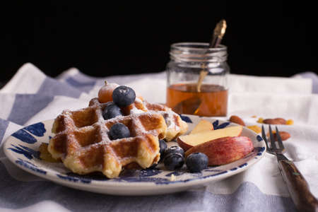 Blueberry apple waffle with honey set on a dish decorated with fresh blueberry, apple, tea pot with copy space.の写真素材