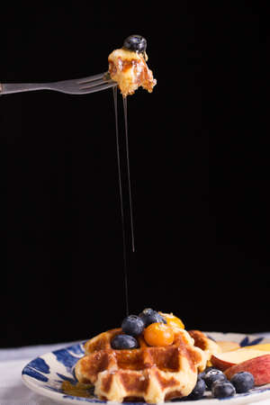 Blueberry waffle set in a nice dish and a fork cut in piece with black background copy space.の写真素材