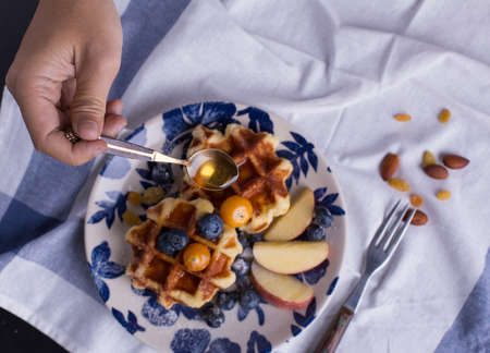Blueberry apple waffle with honey set on a dish with a chef's hand holding spoon for a jar of honey ready to serve.の写真素材