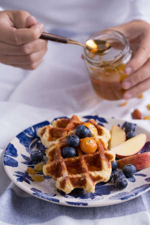 Blueberry apple waffle with honey set on a dish with a chef's hand holding spoon for a jar of honey ready to serve.の写真素材