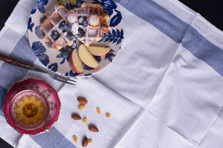Blueberry apple waffle with honey set on a dish decorated with fresh blueberry, apple, tea pot with copy space.の写真素材