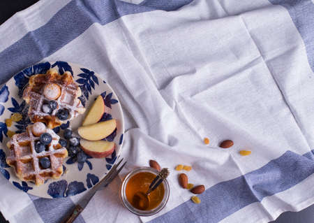 Blueberry apple waffle with honey set on a dish decorated with fresh blueberry, apple, tea pot with copy space.の写真素材