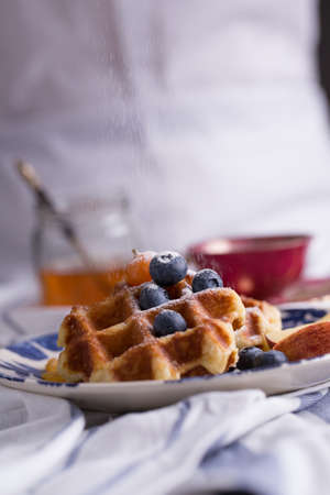 Blueberry apple waffle with honey set on a dish decorated with fresh blueberry, apple, tea pot.の写真素材