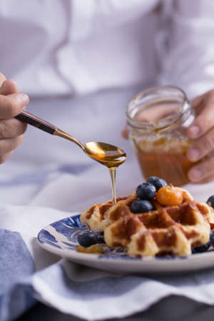 Blueberry apple waffle with honey set on a dish with a chef's hand holding spoon for a jar of honey ready to serve.の写真素材