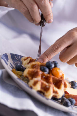 Closeup of a fork cutting a piece of blueberry waffle decorated with fresh blueberry in a nice dish.の写真素材