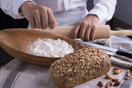 Whole grain bread put on kitchen napkin decorated with almond with a chef holding dough roller at the background.の写真素材