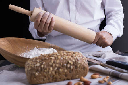 Whole grain bread put on kitchen napkin decorated with almond with a chef holding dough roller at the background.の写真素材