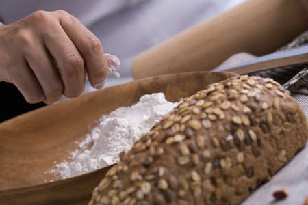 Whole grain bread put on kitchen napkin decorated with almond with a chef holding dough roller at the background.の写真素材