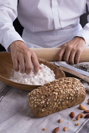 Whole grain bread put on kitchen napkin decorated with almond with a chef holding dough roller at...