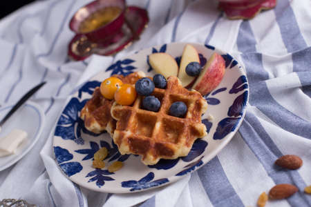 Blueberry apple waffle with honey set on a dish decorated with fresh blueberry, apple and almond.の写真素材
