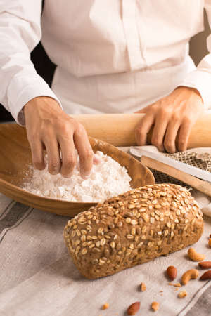 Whole grain bread put on kitchen napkin decorated with almond with a chef holding dough roller at the background.の写真素材