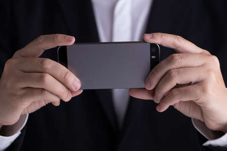 A man in black casual suit holding his mobile phone taking photo.