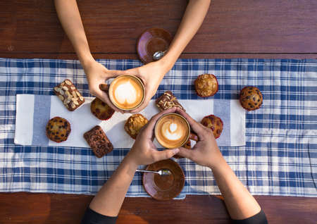 Coffee and cake with hands holding cups of hot latte decorated with muffin and brownies.の写真素材
