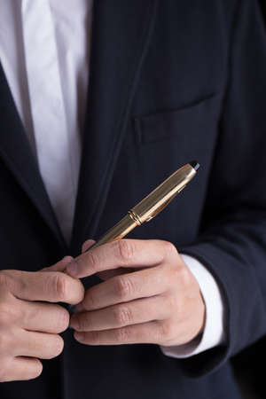 A man in black casual suit holding a gold fountain pen for sign the contract in formal way.の写真素材