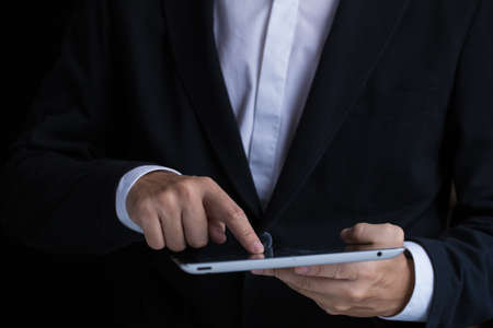 A business man in black suit using digital tablet.の写真素材