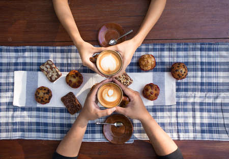 Coffee and cake with hands holding cups of hot latte decorated with muffin and brownies.の写真素材