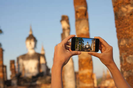 A hand taking photo of Buddha statue with smartphone, Sukhothai, Thailandの写真素材
