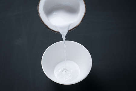 Coconut milk pouring from coconut shell to white bowl on blackboard background.の写真素材
