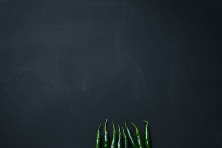 Eight Green chili arranging in line on blackboard background.
