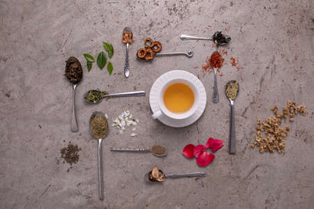 Various ingredient of tea leaf put in many kind of spoon with many kind of leaves and flowers decorated and a cup of tea in the middle.の写真素材