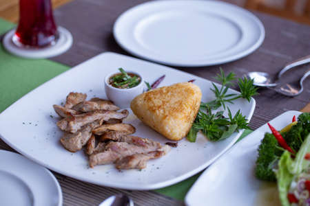 Grilled pork with grilled sticky rice and spicy sauce put on a dish decorated with vegetable on a dining table set.の写真素材