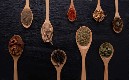 Various kind of dried leaves, fruit and flower put in many kind of wooden spoons on black background.の写真素材