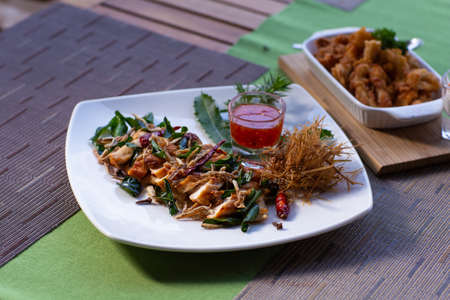 A dish of Thai style fried chicken with side herbs, lemongrass and kaffir lime leaves with sweet sauce on dining table in restaurant.の写真素材