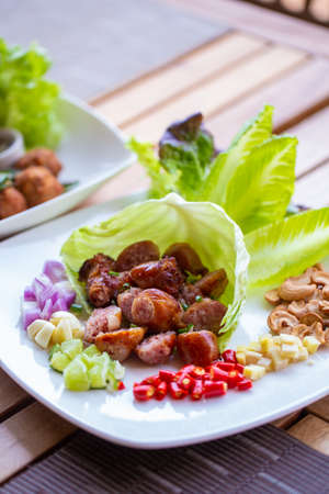 A dish of Thai style fermented sausage with side herbs, chili, lime, ginger, cashew nut. garlic and shallot on dining table.の写真素材