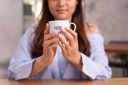 An Asian woman with long hair holding a white cup of tea smiling.の写真素材