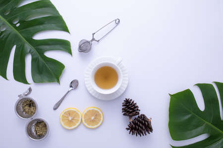 A glass of hot tea with fruit, tea infuser, spoon and leaves decorated on white background.の写真素材