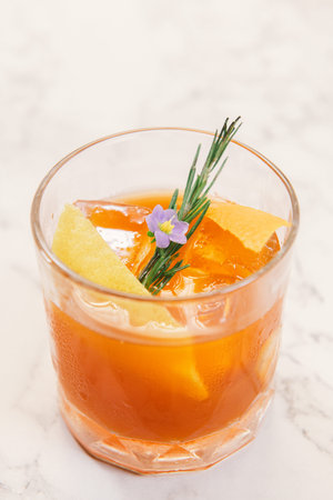 Orange color cocktail in a rocks glass decorated with orange peel, rosemary and purple flower.の写真素材