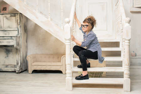 Beautiful young girl in glasses sitting on the stairs of the bright roomの写真素材
