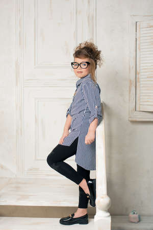 Beautiful young girl in glasses sitting on the stairs of the bright roomの写真素材